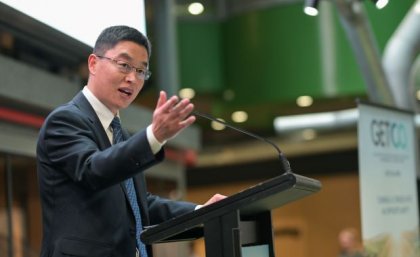 A man stands at a lectern with his hand raised.